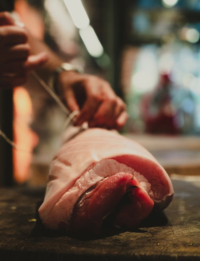 A close-up view of a raw pork cut being tied with string by hands in a warm, inviting kitchen setting.