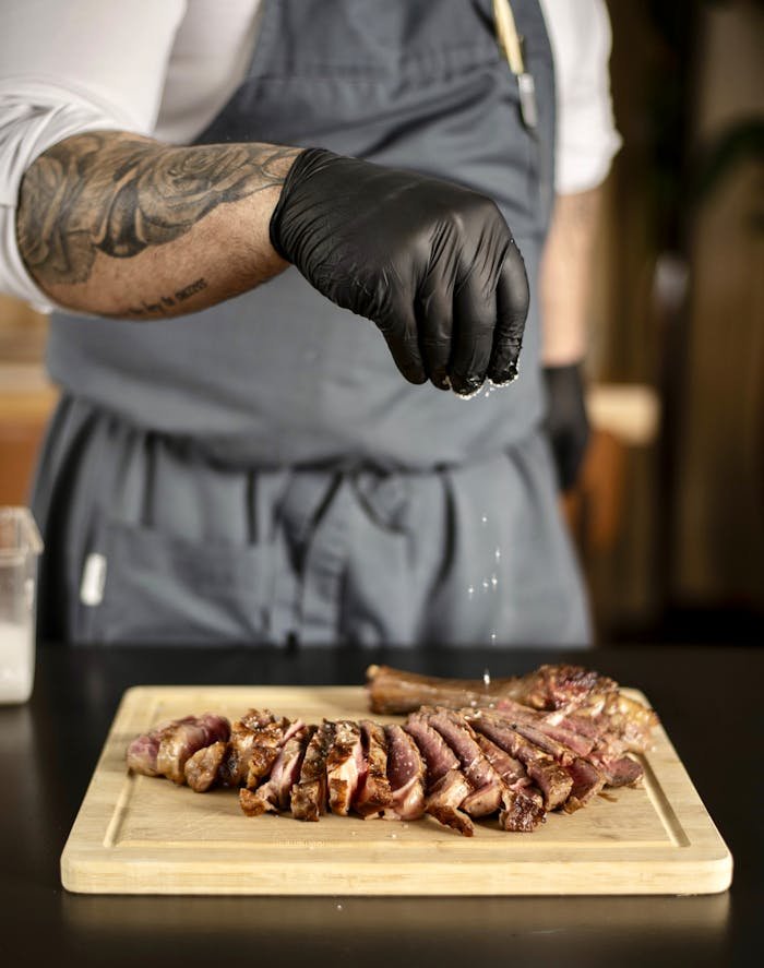 service-03 A chef seasons grilled meat slices on a cutting board with salt.