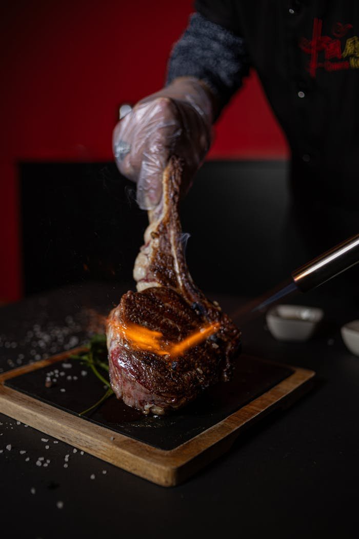 A chef expertly sears a Tomahawk steak with a torch, creating a delicious caramelized crust.